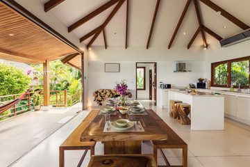 Luxury interior design in living room  villa. Bright space with high raised ceiling and wooden dining table. Simple asian style lunch, orchids in glass bottle