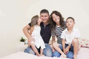 Portrait of Happy Caucasian Family with Two  Kids Posing Together Embraced and Smiling Happily. Girl Kissing Her Father.