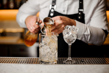 Bartender adding alcoholic drink into a glass filled with ice cubes