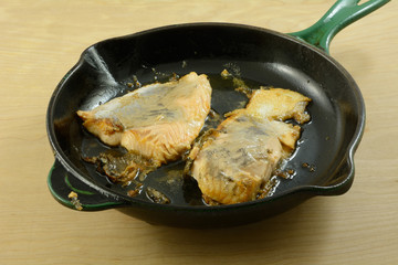Two salmon fillets sauteed in olive oil in well seasoned cast iron frying pan skillet