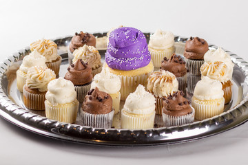 Platter of small cupcakes with large purple one in the center.