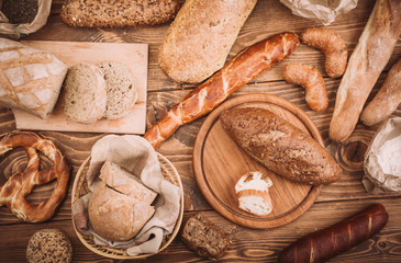 Many mixed baked breads and rolls on rustic wooden table