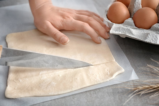 Woman cutting flaky dough on table, closeup