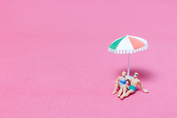 Miniature people wearing swimsuit relaxing on pink background