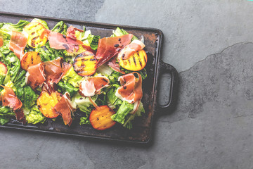 Lettuce, ham serrano and grilled peaches salad served on black board. Top view