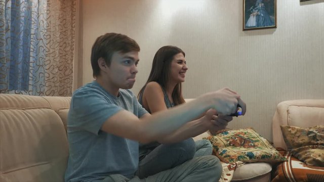 A girl and a guy play a game console. They hold the joysticks in their hands. They are sitting on the couch in the room. Portrait of happy excited family playing video games