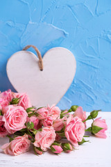 Tender pink roses flowers and white heart on  light blue textured background.