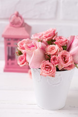 Pink roses flowers  in white pot and pink lantern against  white brick wall.