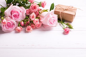 Tender pink roses flowers  and  wrapped box with present on white wooden background.
