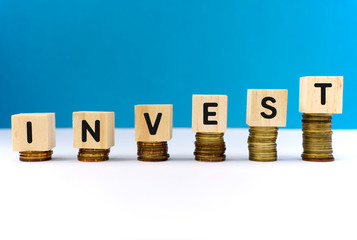 Invest word on wooden block on top of coins stack