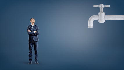 A small businessman looks up to a giant metal faucet on a dark blue background.