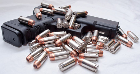 A black semi automatic pistol with .40 caliber hollow point bullets laying on the gun and next to it. Shot with a white background