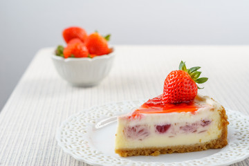 Delicious cheesecake with strawberry on a table against white wall.
