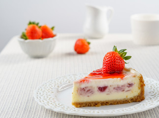 Delicious cheesecake with strawberry on a table against white wall.