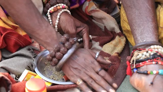 Hindu sadhu man preparing a cigarette to smoke marijuana with chillum on the ghats of the Ganges river in Varanasi, India . Close up
