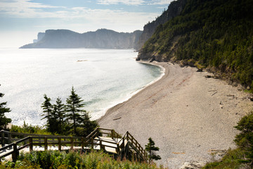 A walkway leading down to a beautiful beach with blue water and green trees on the surrounding mountainous landscape