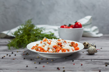 delicious rice with stewed carrots, peas and onions on a white plate, quail eggs, bowl with cherry tomatoes, towel, pepper and dill on a light wooden table