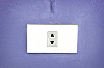 Electric plug socket on violet pastel wall.