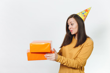 Beautiful caucasian fun young happy woman in yellow clothes, birthday party hat holding orange gift boxes with present, celebrating and enjoying holiday on white background isolated for advertisement.
