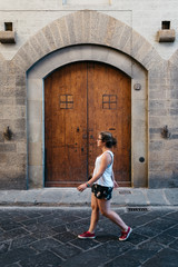 Fototapeta na wymiar Young woman walking on the street against old arch door