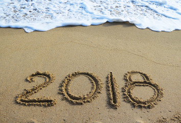 New Year 2018 is coming concept - inscription 2017 and 2018 on a beach sand, the wave is starting to cover the digits 2018