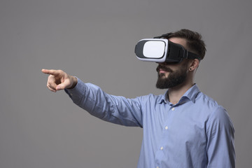 Side view of business man wearing vr glasses outstretching hand and pointing finger on interactive touch screen over gray background with copyspace