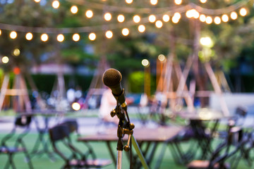 Microphone stand for the singer with the light hanging and table set for party in the park...