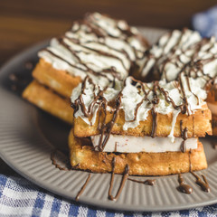 waffles with cream and chocolate on plate on wooden table.