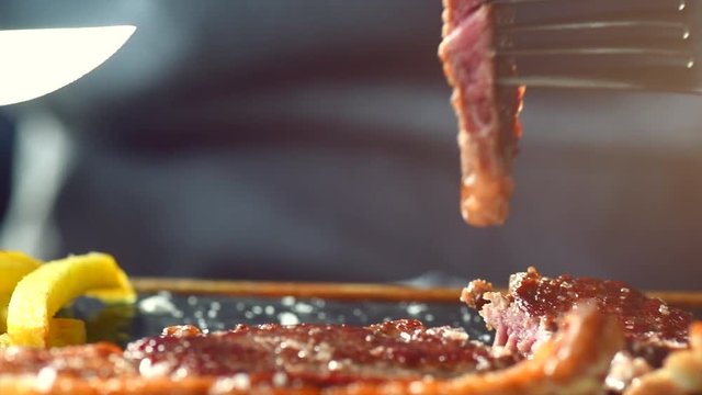 Grilled steak closeup. Person eating juicy roasted beef steak with vegetables and fries. Slow motion 4K UHD video footage. 3840X2160