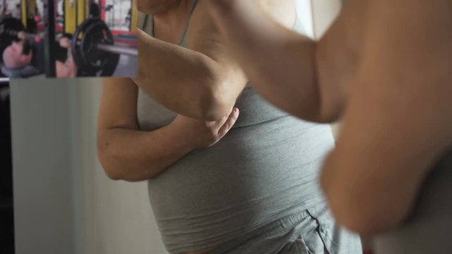 Plump man looking at muscular athlete on photo and touching his fat belly