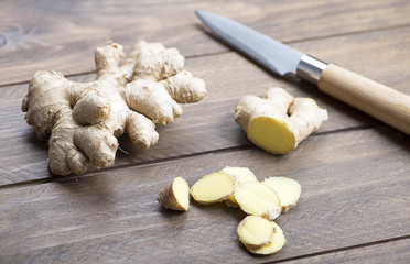 Ginger next to kitchen knife on wooden table. Food