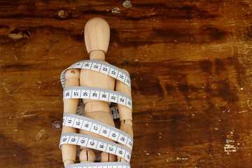 Ball-jointed doll wrapped with tape measure on wooden background. Concept of weight management