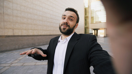 Young bearded businessman talking smartphone having online video chat business meeting outdoors