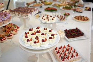 Restaurant catering table full of different types of desserts: creamy pieces of cakes and souffle,secorated with strawberry and chocolate.