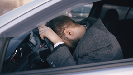 Young bearded business man sitting in car very upset and stressed after hard failure and moving in traffic jam