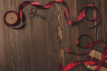 flat lay with arranged red ribbon, present and scissors on wooden surface