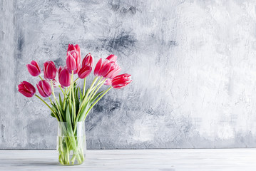 Bouquet of pink tulips in a glass vase  on grey background.