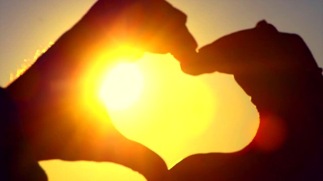 Valentine's Day. Person making heart with hands over nature sunset background. Silhouette hand in heart shape with sun inside. Slow motion 4K UHD video footage. 3840X2160