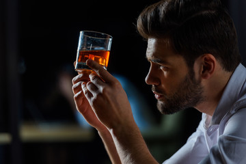 side view of handsome businessman looking at glass of whiskey