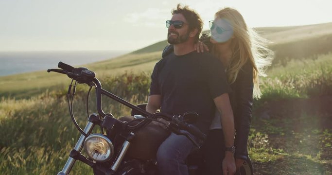 Attractive couple on vintage motorcycle watching the sunset