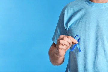 Young man holding blue ribbon on color background, closeup. Prostate cancer awareness concept