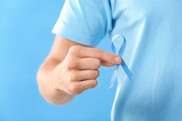 Young man holding blue ribbon on color background, closeup. Prostate cancer awareness concept
