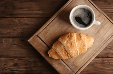 Board with yummy fresh croissant and cup of coffee on wooden table