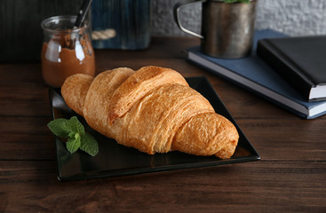 Plate with yummy fresh croissant on wooden table