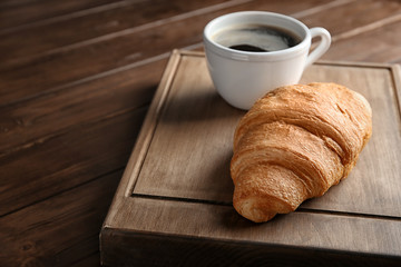 Board with yummy fresh croissant and cup of coffee on wooden table