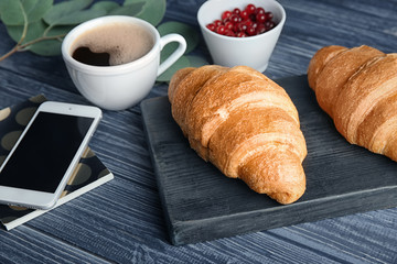 Composition with yummy fresh croissants and mobile phone on wooden table