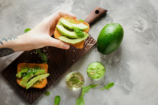 Woman Holding Delicious Avocado Toast Over Table, Top View
