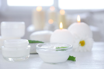 Bowl with body cream and aloe leaves on table