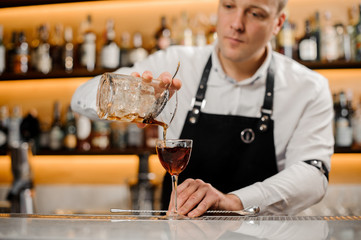 Young bartender adding alcoholic drink into an elegant glass