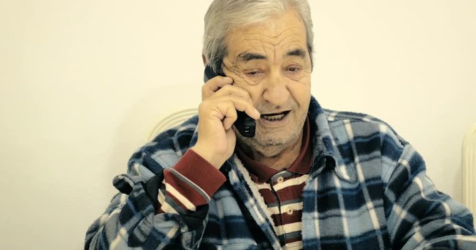 Close-up grandfather of eighty-two years talking to his friend on the phone sitting on a chair in the room.
